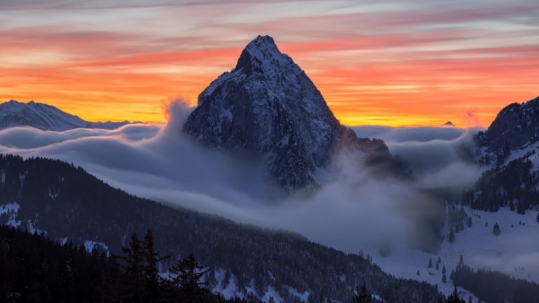 The Swiss Furggelen alp with fog surrounding its base and a colorful sunrise behind it