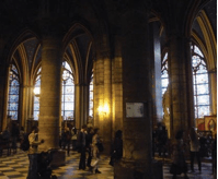 A photograph of a large room inside Notre Dame with stained-glass windows along one wall and concrete support beams throughout.