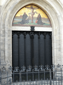 A picture of a depiction of Jesus on the cross above two black doors on the outside of the Wittenburg Church.