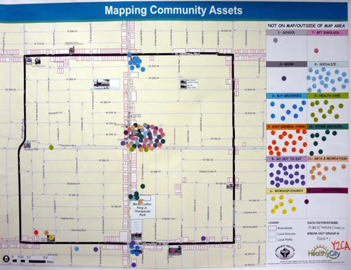 Map labeled Mapping Community Assets that shows color coded dots that represent different assets. Multiple color coded dots in the center of the map surrounded by thick black outline of community that encompasses all colored dots.