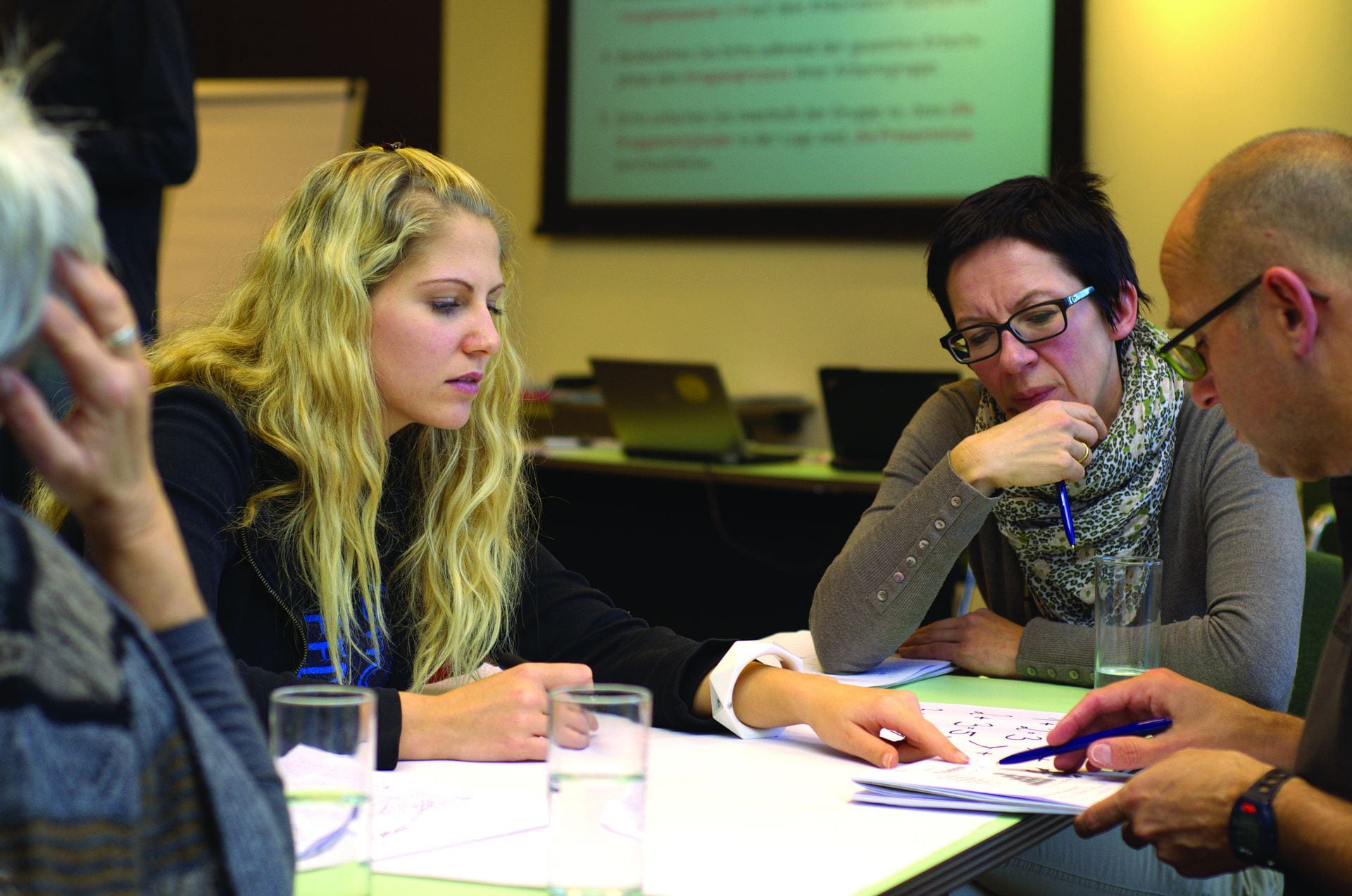 Three employees discuss diagrams across a table.