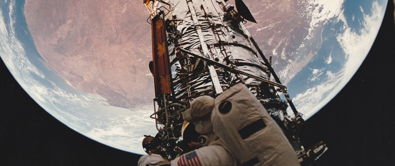 Southern Summer. In this fish-eye view from the Space Shuttle Atlantis, a portion of the Hubble Space Telescope is seen against the reddish outback of western Australia.